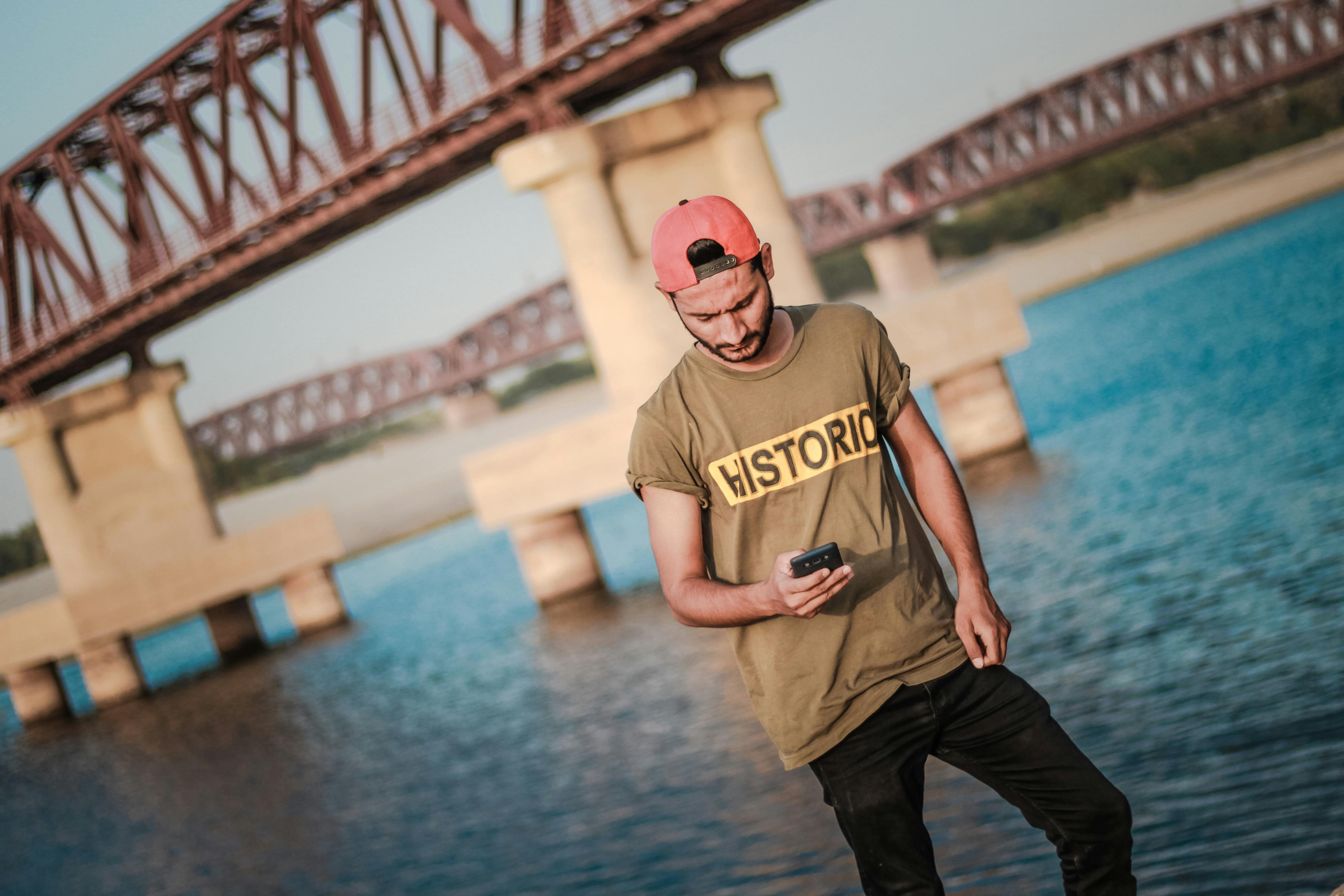 年轻人在河桥旁拿着智能手机休闲，享受夏日的户外时光