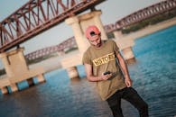 年轻人在河桥旁拿着智能手机休闲，享受夏日的户外时光