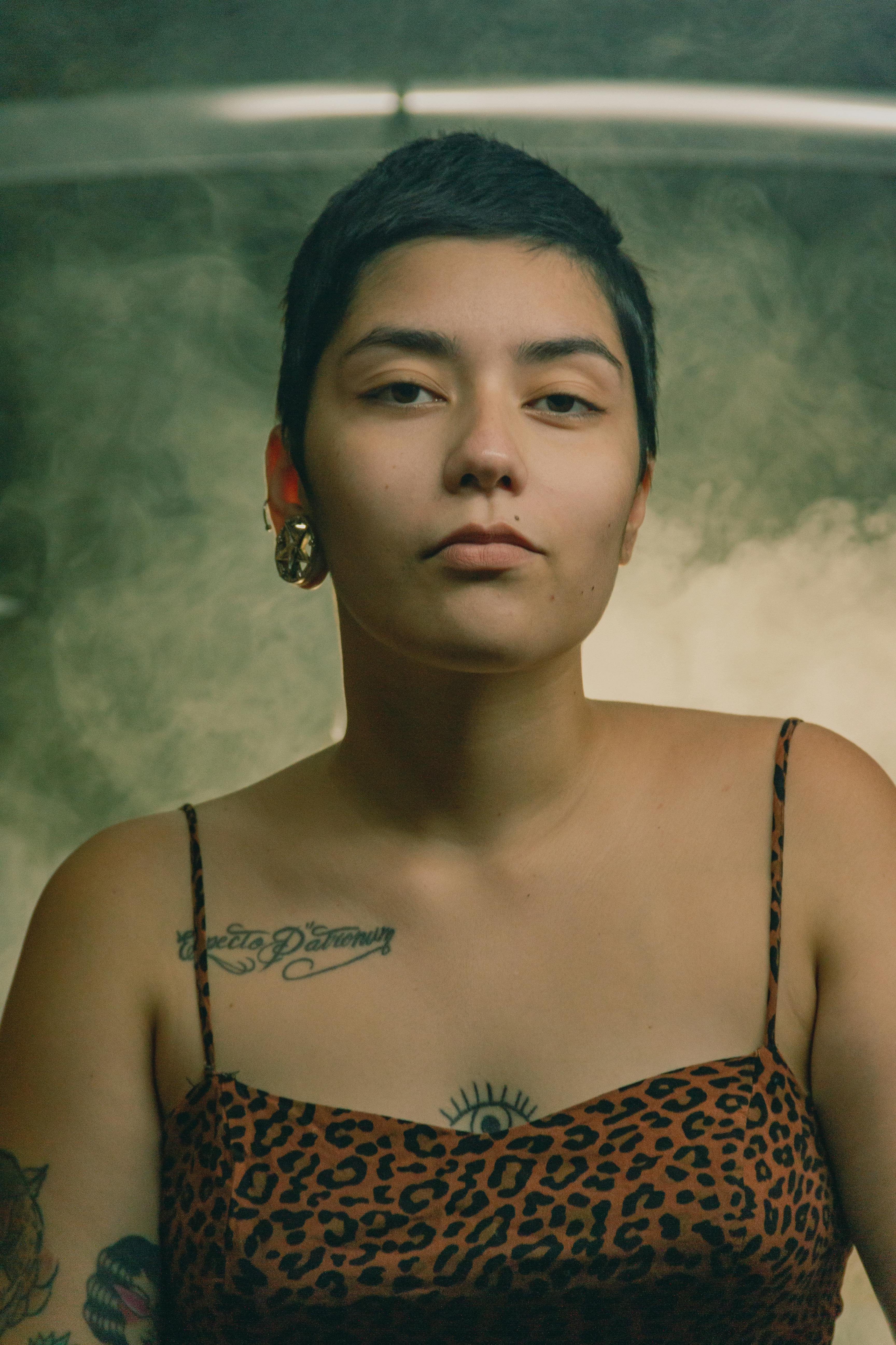 Moody portrait of a tattooed woman with short hair and leopard print dress.