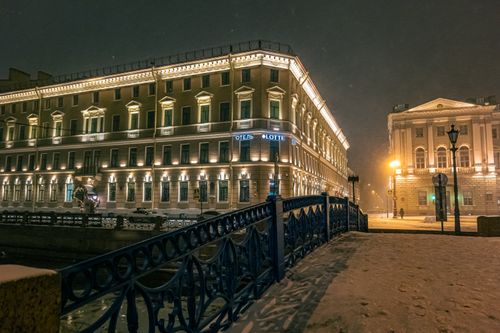 Free A beautifully illuminated hotel on a snowy winter night in Saint Petersburg, showcasing classic architecture with street lights and snow. Stock Photo