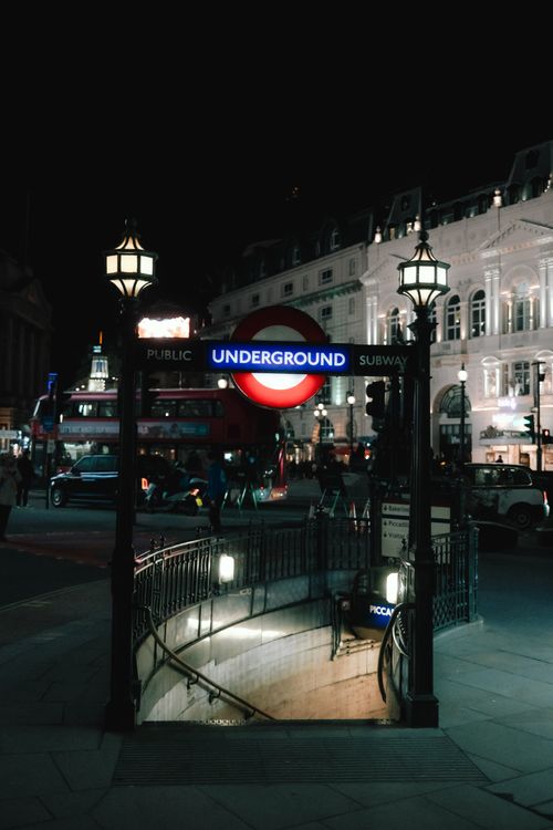 Free Night scene of an illuminated London Underground entrance with city lights and bustling streetlife. Stock Photo
