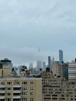 Fog envelops the New York City skyline, showcasing towering skyscrapers during the day.