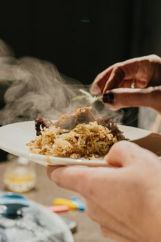 Close-up of a steaming meat and rice dish being garnished.