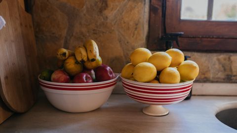 Colorful bowls filled with fresh bananas, apples, and lemons on a rustic kitchen counter.