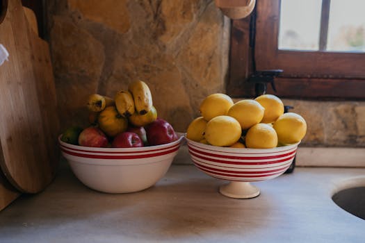 Colorful bowls filled with fresh bananas, apples, and lemons on a rustic kitchen counter.