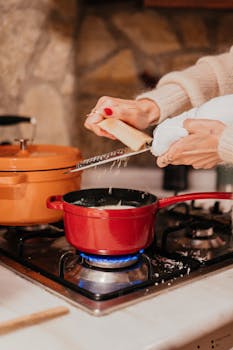 A person grates cheese over a steaming red pot on a stove, showcasing culinary preparation.