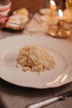 Close-up of pasta with creamy sauce under a warm candlelit setting, creating a cozy dining experience.
