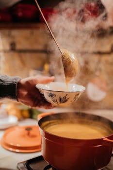 A warm, comforting scene of steaming soup being ladled into a bowl in a cozy kitchen setting.