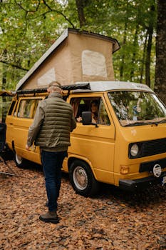 A man stands by a yellow camper van in a lush autumn forest setting.