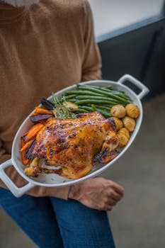 A person holding a platter of roasted chicken with vegetables, perfect for a balanced meal.
