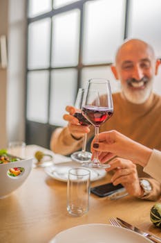Senior man smiling and toasting with red wine, enjoying a meal indoors.