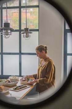 A woman preparing a meal on a kitchen counter with various dishes, seen through a circular window.
