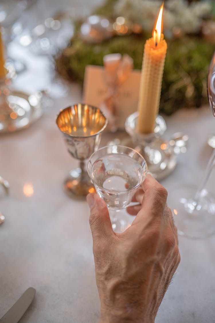 A Person Holding A Water Goblet At A Dinner Table