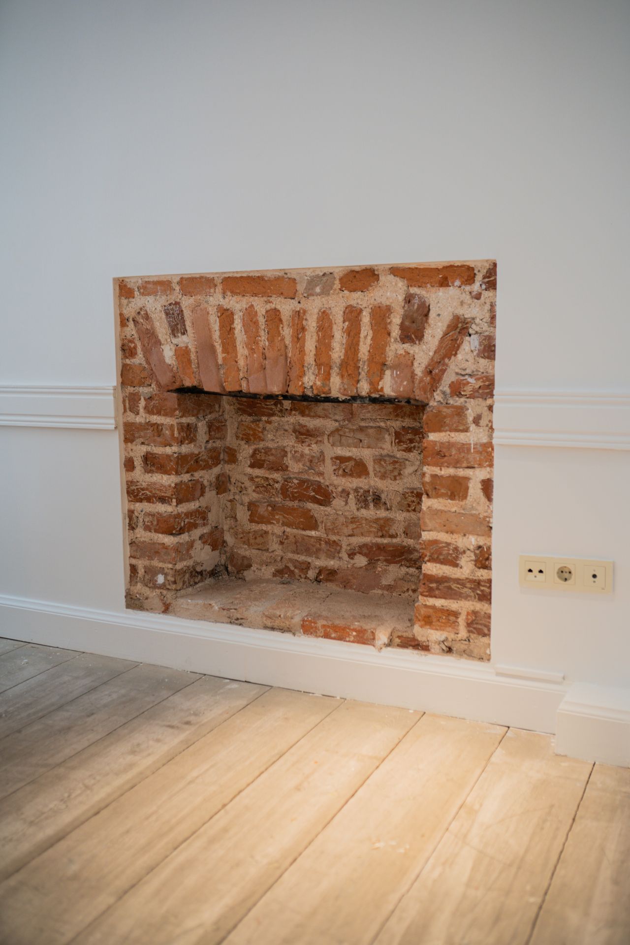 Exposed red brick fireplace surround in a white room with wood floor