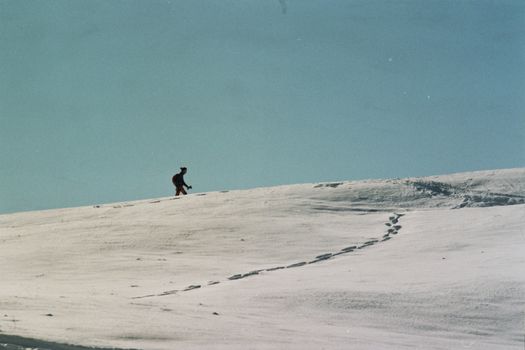 A lone hiker traverses the snow-covered hills of Piani di Artavaggio, Italy.