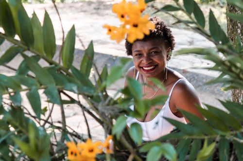 Free Joyful woman smiling behind vibrant yellow flowers surrounded by greenery. Stock Photo