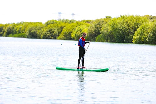 Man in Blue and Red Life Vest Standing on Green Kayak