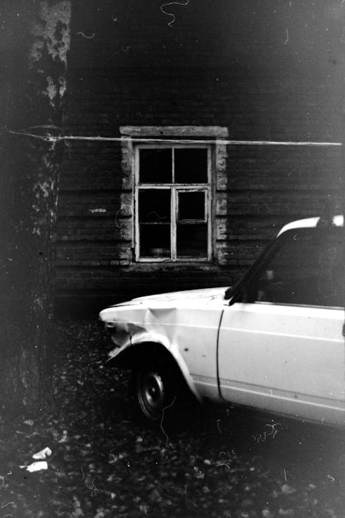 White Car in Front of Wooden Hut in Black and White