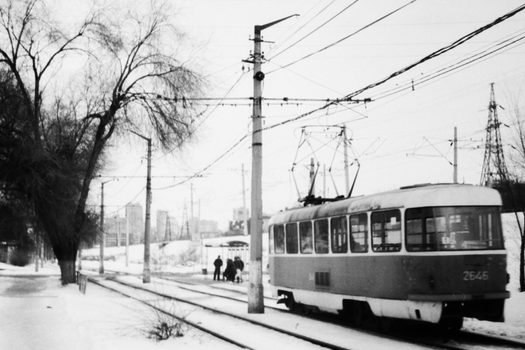 Tram navigating snowy urban streets in black and white winter scene.