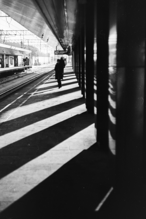 Free Black and white image of a person walking in an urban train station with dramatic shadows. Stock Photo