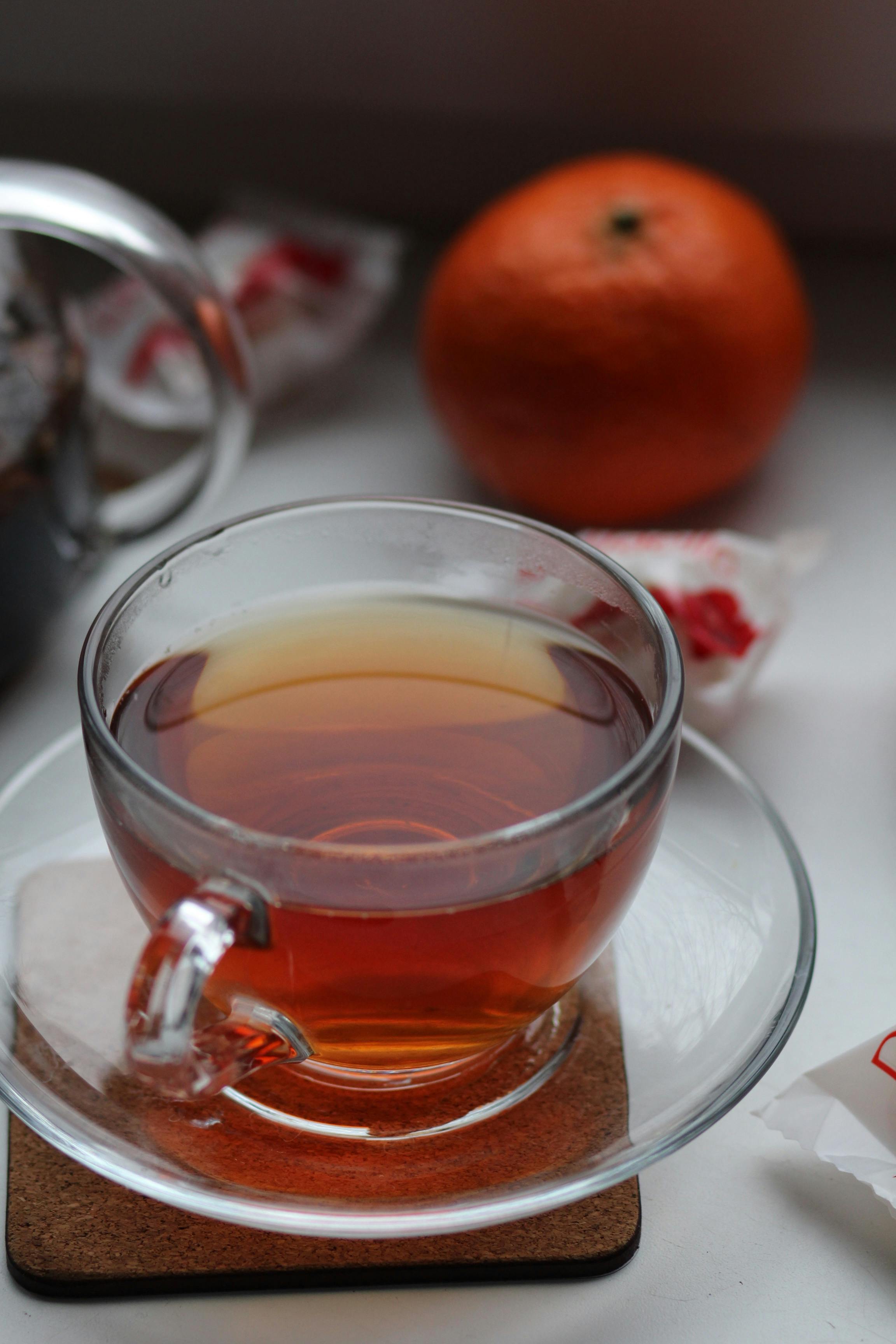 A steaming cup of orange blossom tea with visible steam rising, set against a backdrop of blurred orange blossoms.