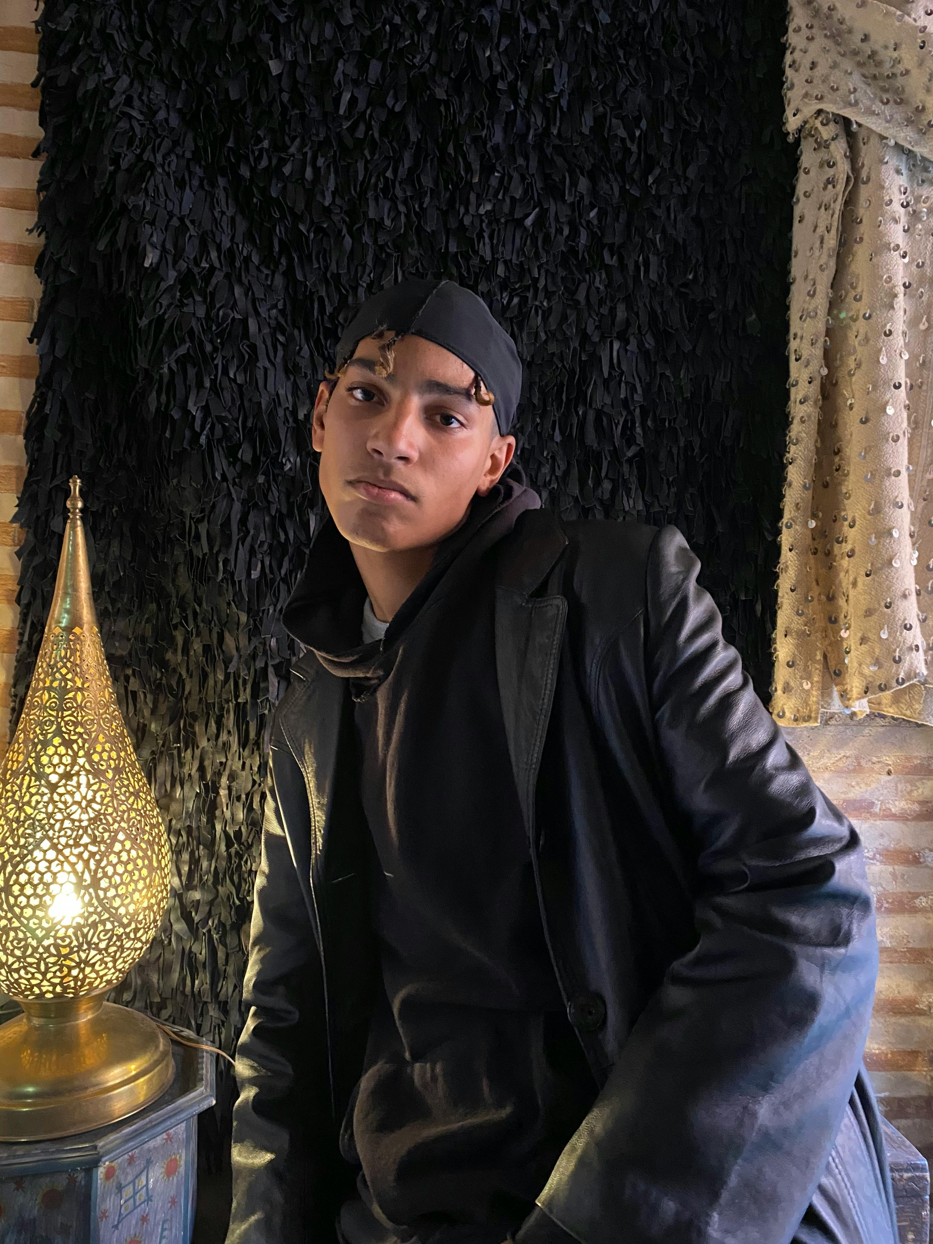 Free Young man in a black leather jacket posing indoors with a stylish lamp. Stock Photo