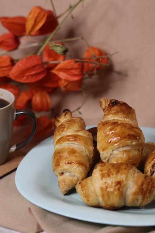 Free Close-up of fresh croissants on a plate with a cup of coffee and red flowers. Stock Photo