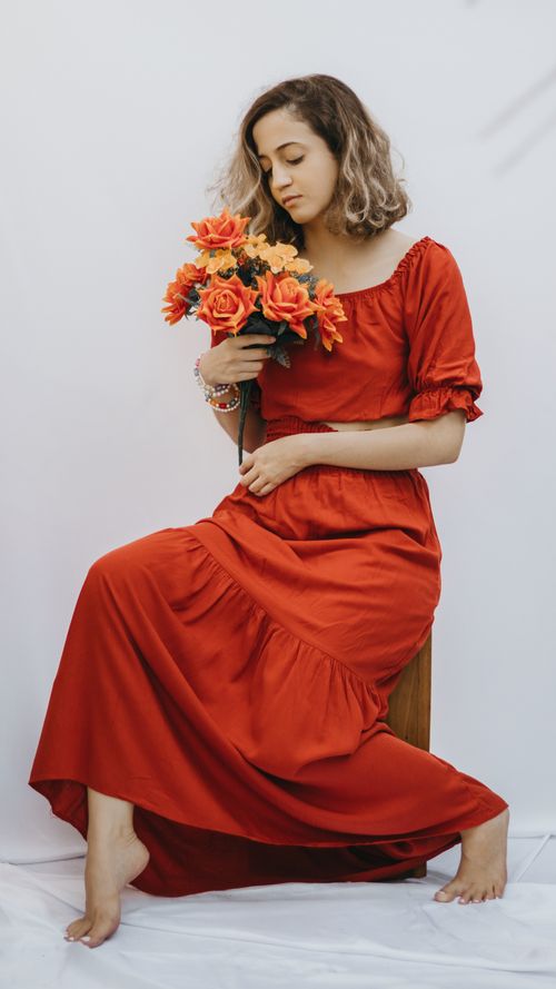Free Elegant woman in a long red dress sitting with a bouquet of orange roses against a white background. Stock Photo