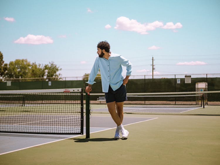 Man Leaning On Net On Empty Tennis Court