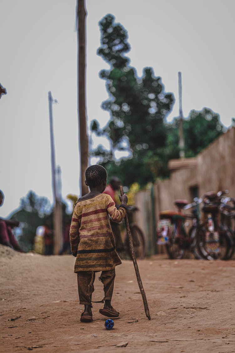 A Boy Walking With A Stick