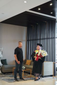 Graduating woman in cap with flowers in modern interior with male companion. - Fotografer Sidoarjo