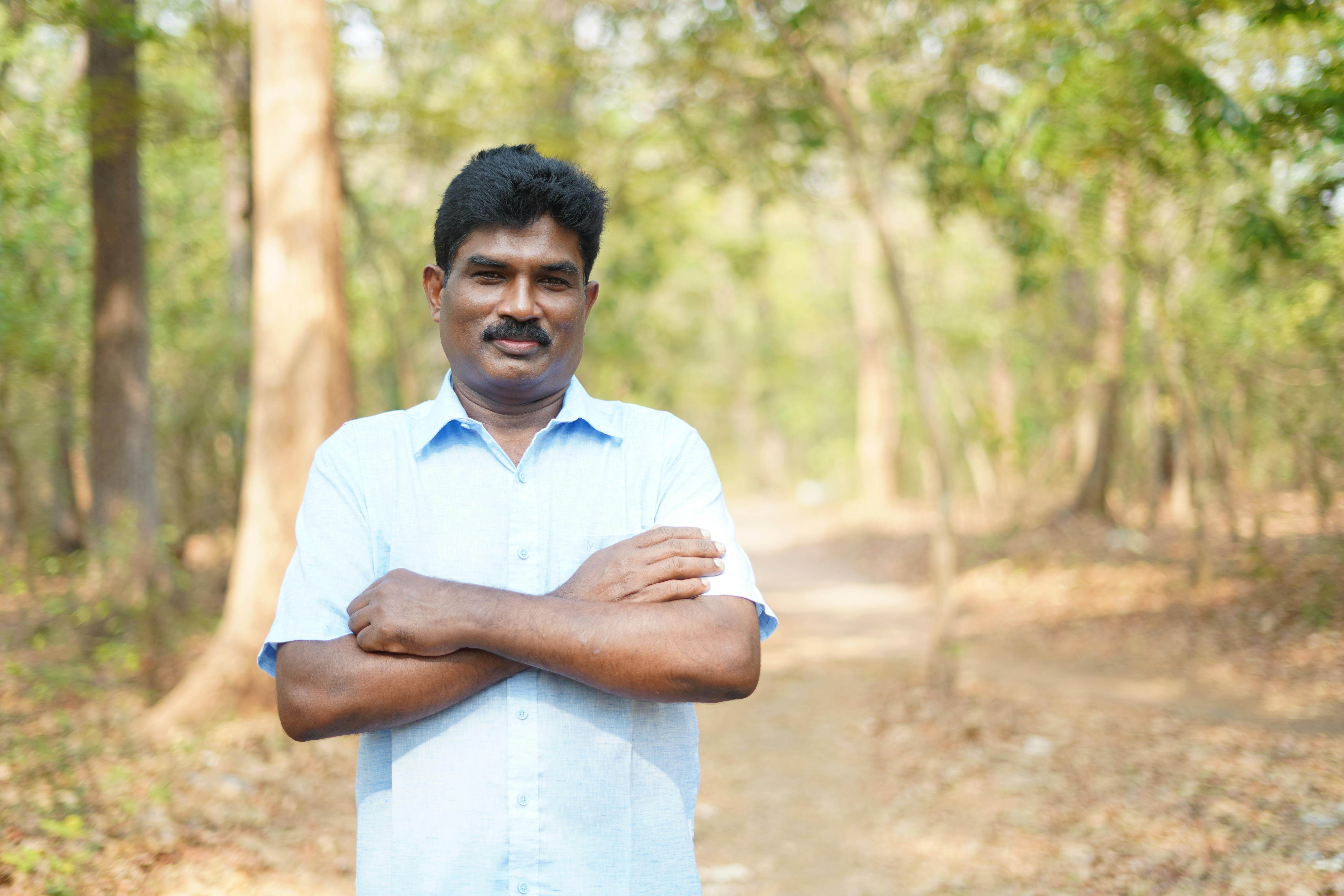 A happy man with a short sleeve shirt stands confidently in a sunlit forest path.