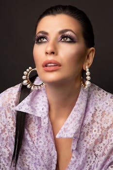 Sophisticated studio portrait of a woman with bold makeup and pearl earrings in elegant lace attire.