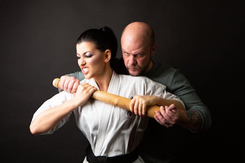 Free A Woman in Karate Uniform and a Man in Green Sweater Fighting With a Wooden Bat Stock Photo