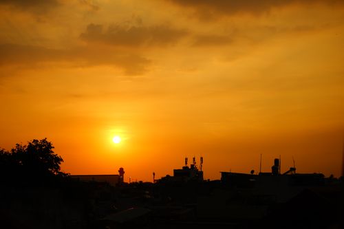 Free Silhouetted city skyline with a vibrant orange and golden sunset, creating a dramatic visual effect. Stock Photo