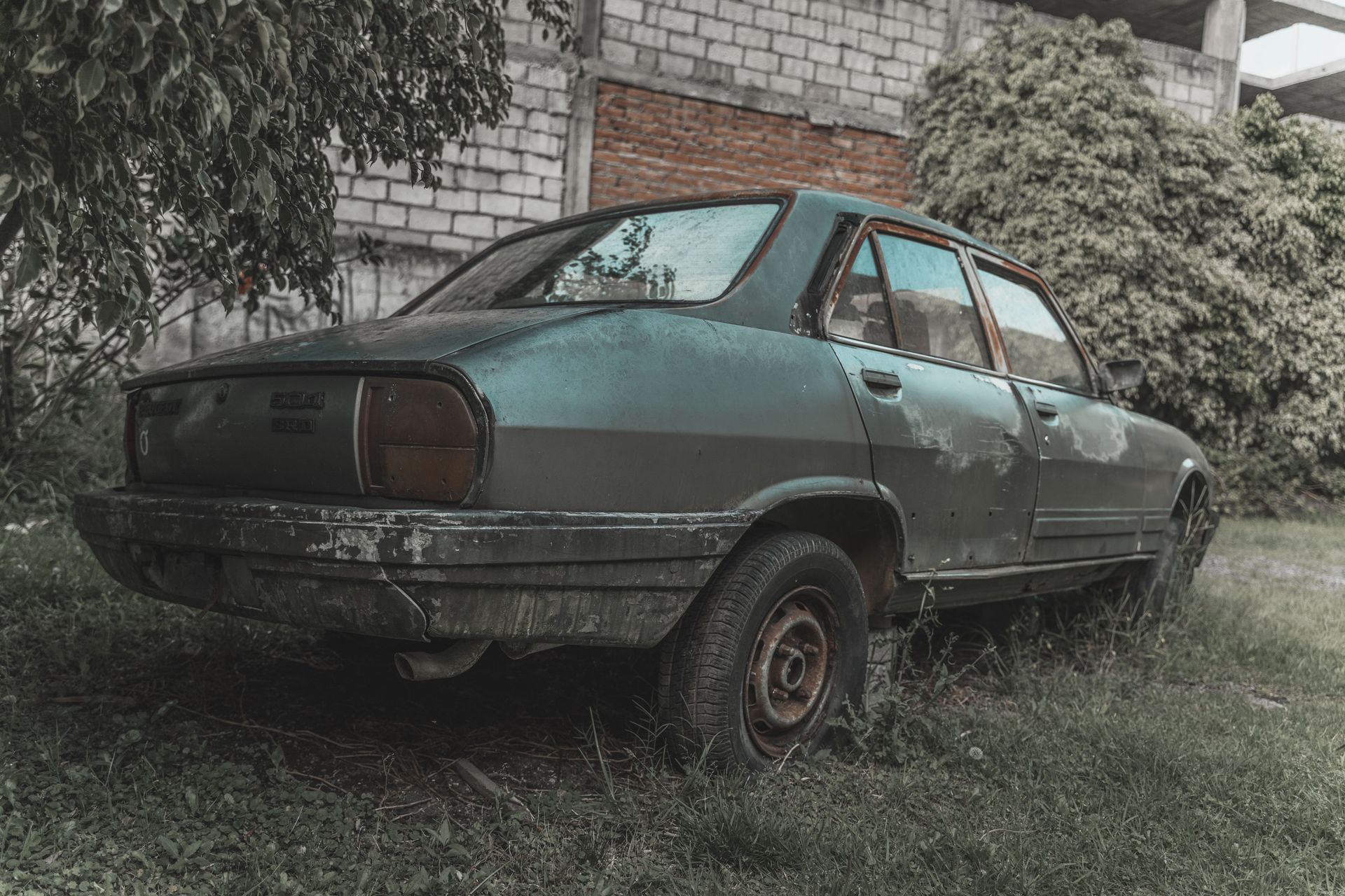 A rusted, old car sits abandoned amidst overgrown grass, embodying decay and nostalgia.