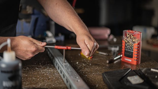 Close-up of hands using hand tools on metal in a workshop setting.