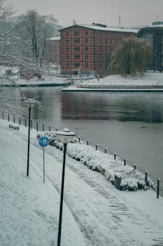 A serene winter scene at the riverside in Bydgoszcz, Poland with snow-covered paths and a red brick building.