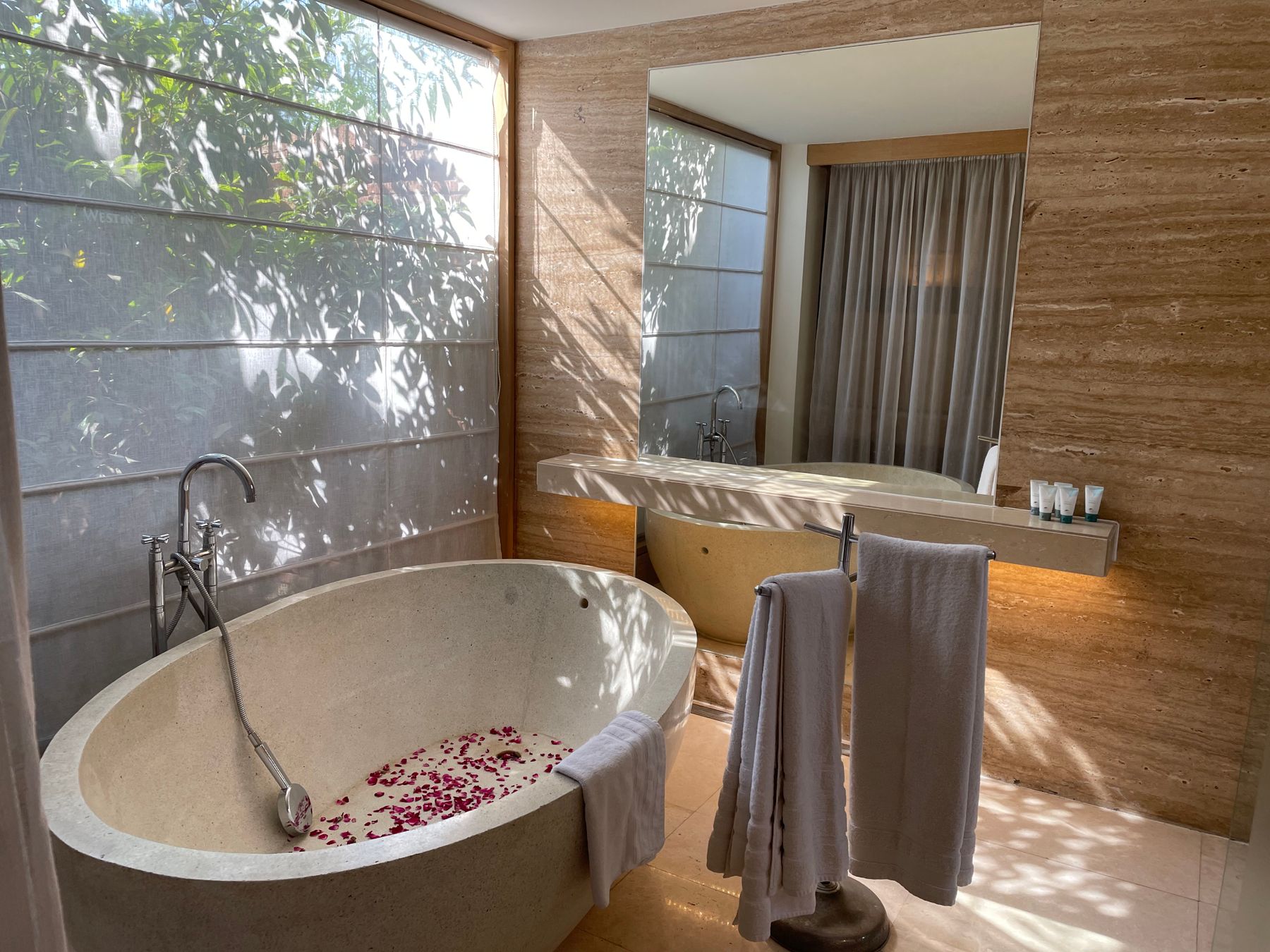 Minimalist bathroom with substantial stone bathtub, towels and natural light