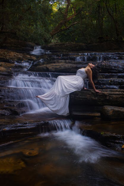 a woman in a white dress is doing yoga in front of a waterfall 27610961  Stock Photo at Vecteezy
