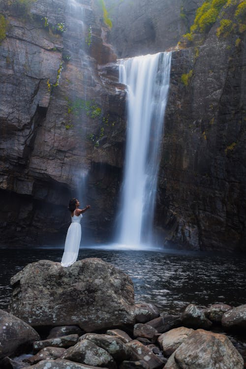 Woman in White Dress Standing on Rock Near Waterfalls