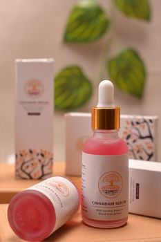 Close-up of a Cinnabari Serum bottle with packaging, set against a leafy background.