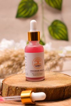 Close-up of pink serum bottle on rustic wood, surrounded by greenery for a natural beauty vibe.