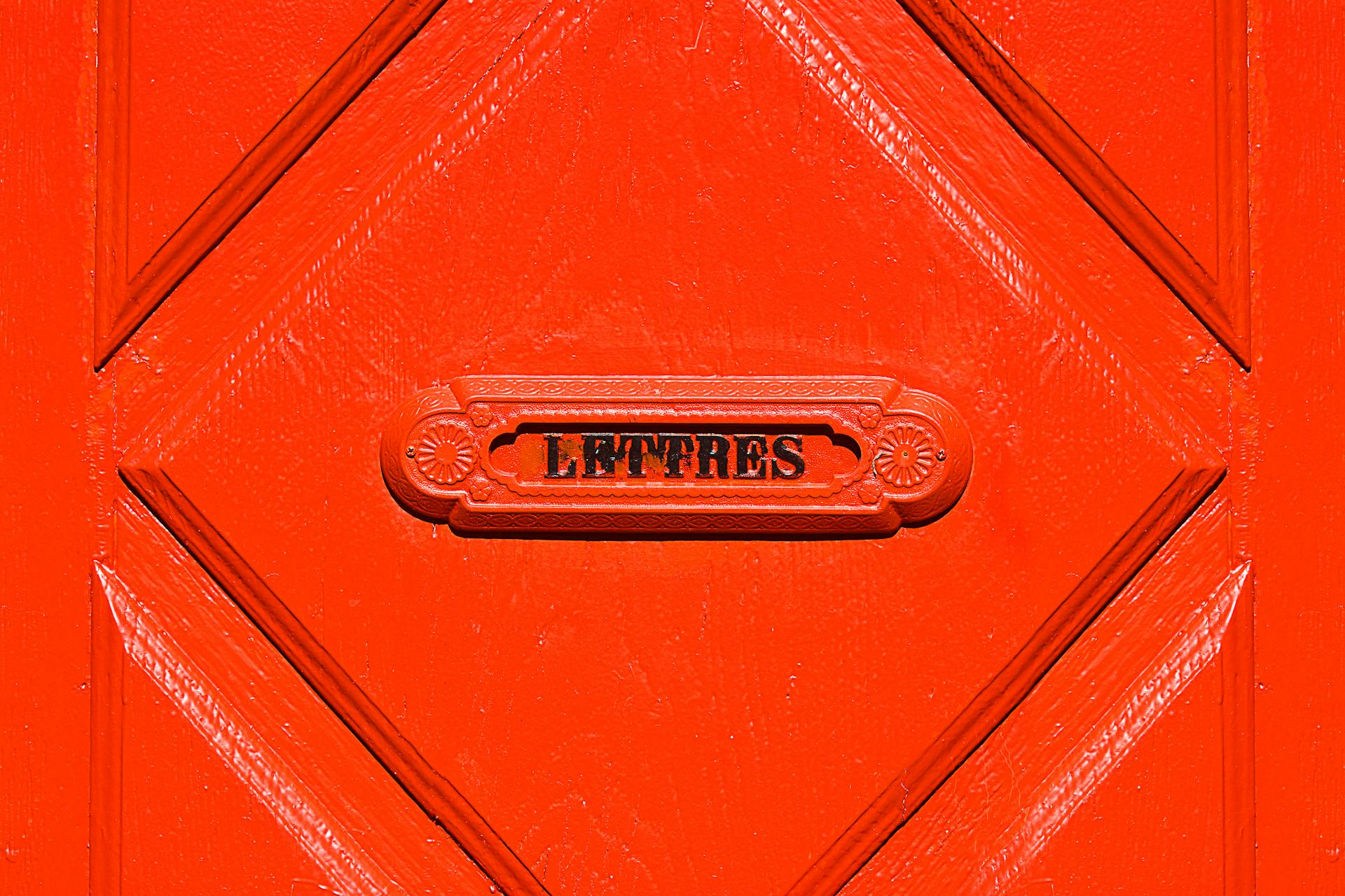Close-up of a vibrant red door featuring a vintage mail slot labeled 'LETTERS'.