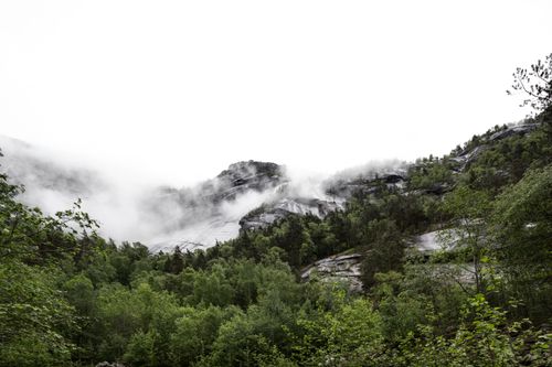 Free A breathtaking view of misty mountains and a lush green forest underneath a cloudy sky. Stock Photo