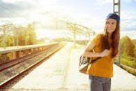 在阳光明媚的火车站，一位微笑的年轻女子背着背包，享受着夏日旅行的氛围