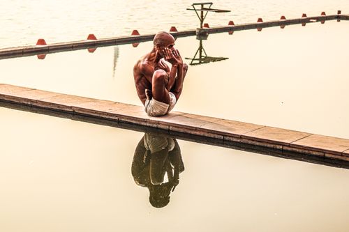 Free Shirtless man doing yoga pose by the water, with serene reflection and peaceful ambiance. Stock Photo