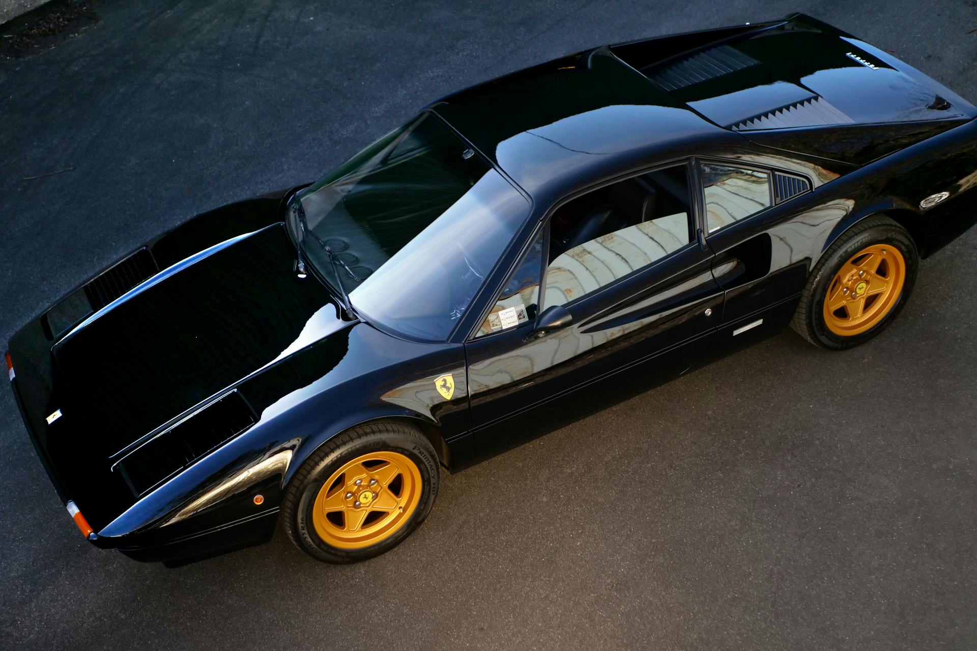 High angle view of a sleek black sports car with striking gold rims on an outdoor pavement.