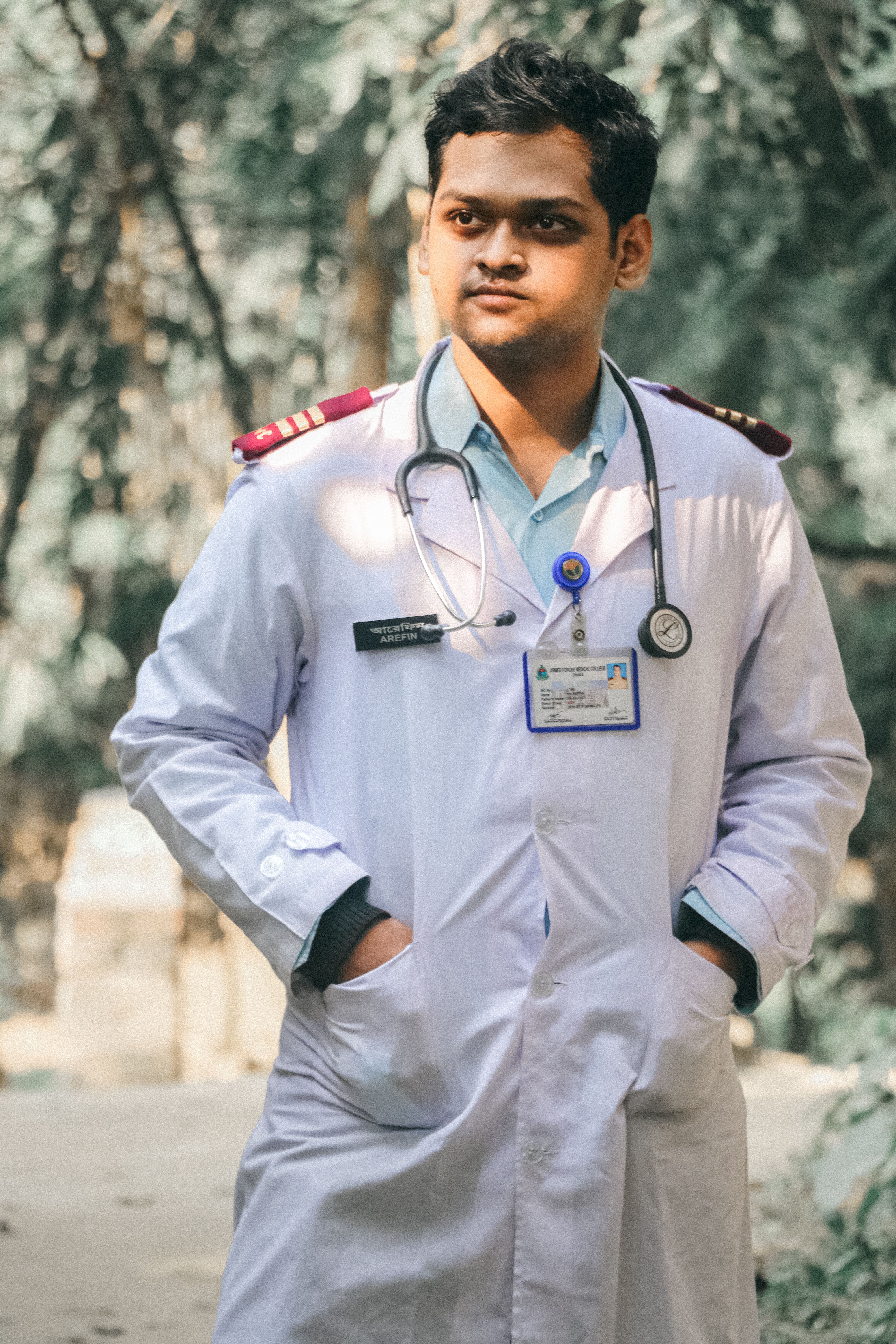 A focused South Asian doctor in a lab coat with a stethoscope around his neck outdoors.