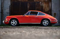 一辆老式橙色汽车停在城乡结合部的背景下，侧面视角凸显了其时尚设计